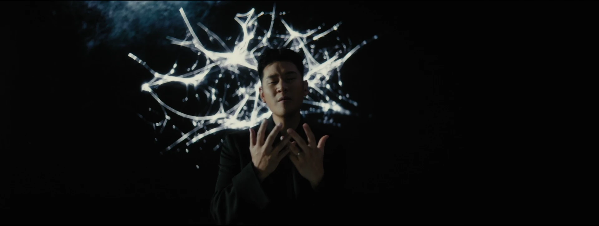 Eric Chou brings his hands to his chest, framed by branching white light.