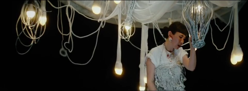 Waa Wei in profile beneath a white suspended structure and hanging bulbs.