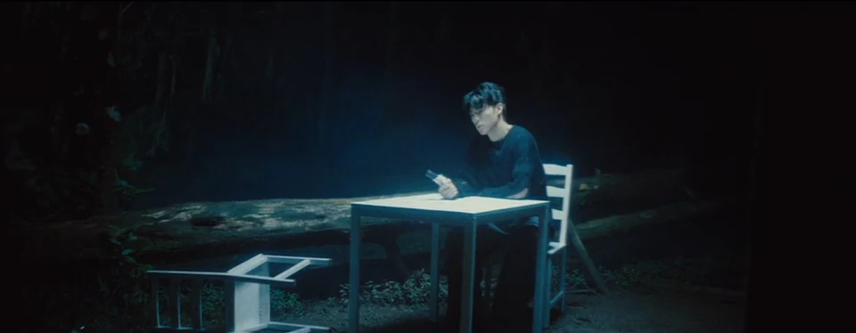 A lone figure at a table among the trees.