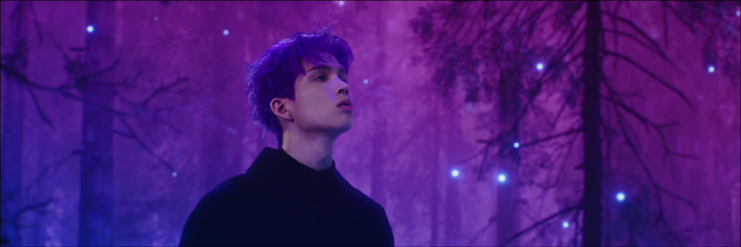 Patrick Brasca looks upward amid glowing trees in the purple forest.