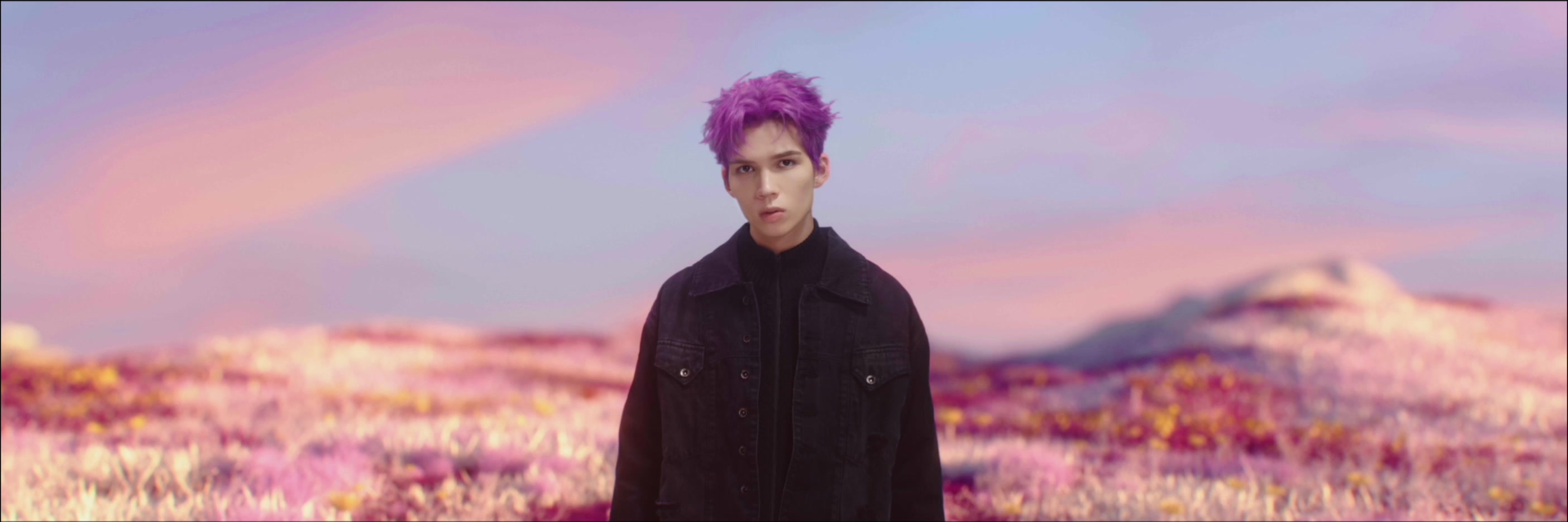 Patrick Brasca stands in a colorful flower field beneath a pink evening sky.