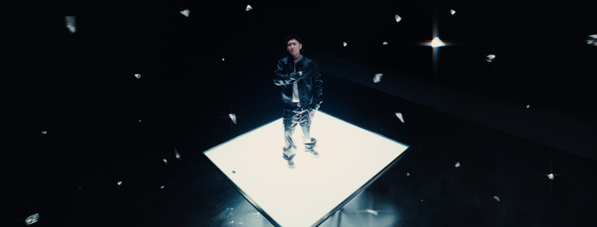 A solo performer stands on a luminous square platform surrounded by floating fragments.